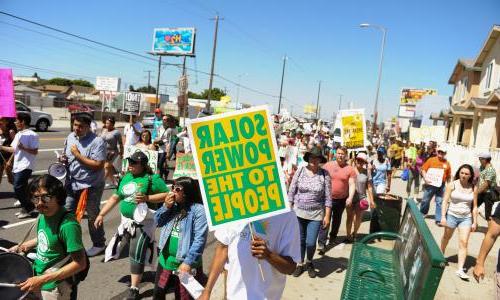 A group of people marching with a sign that reads "太阳能发电 to the people."